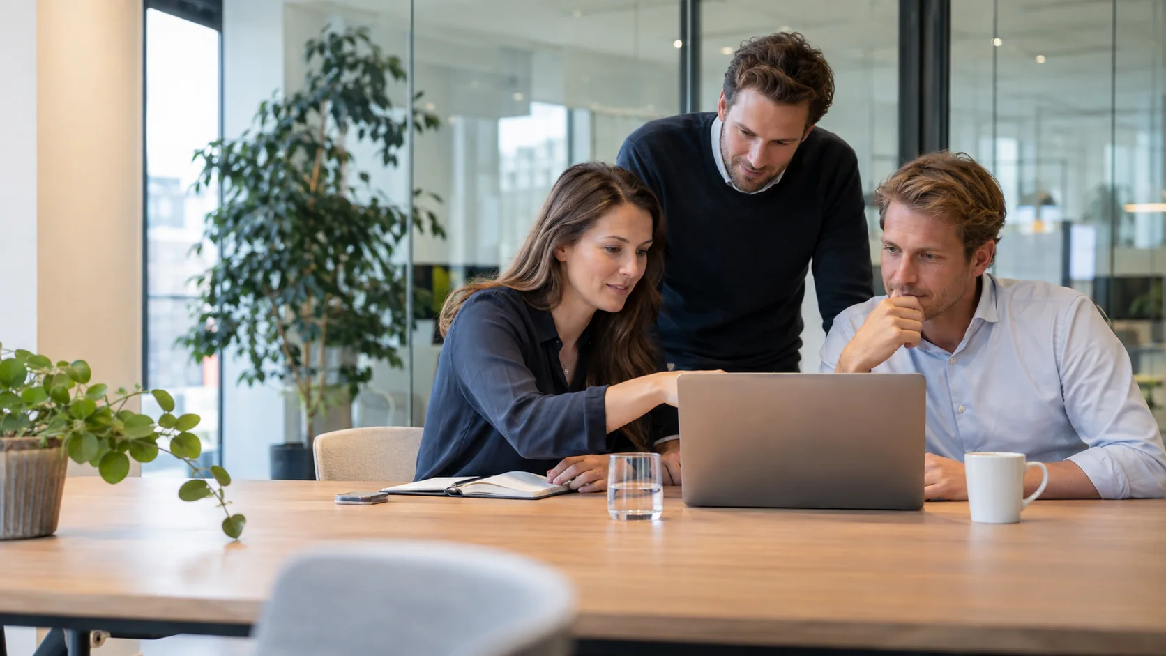 Collega?s bekijken samen klantinformatie op een laptop in een modern kantoor.